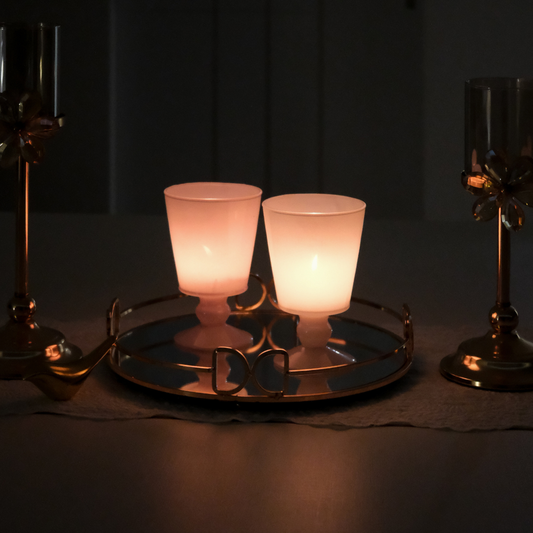 Two lit candle holders on a round mirrored tray, styled on a table with candlesticks in a dark indoor setting.