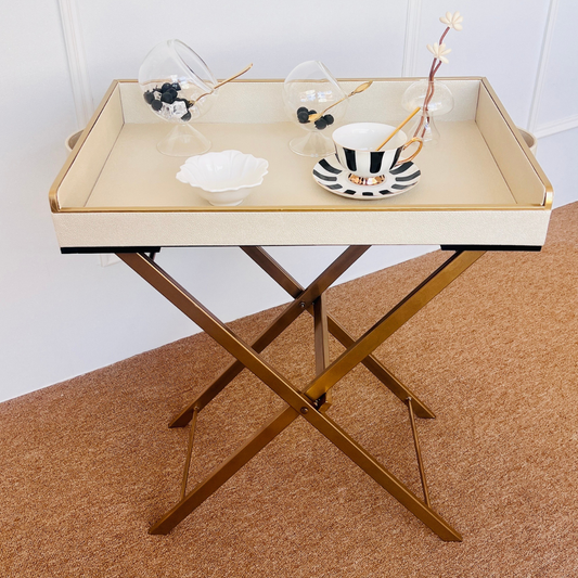 Foldable table with a white butler tray holding decorative items on a brown surface.