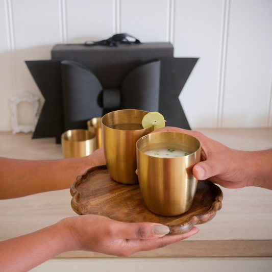 Two big gold glasses with lemon juice and buttermilk placed on a scalloped wooden tray