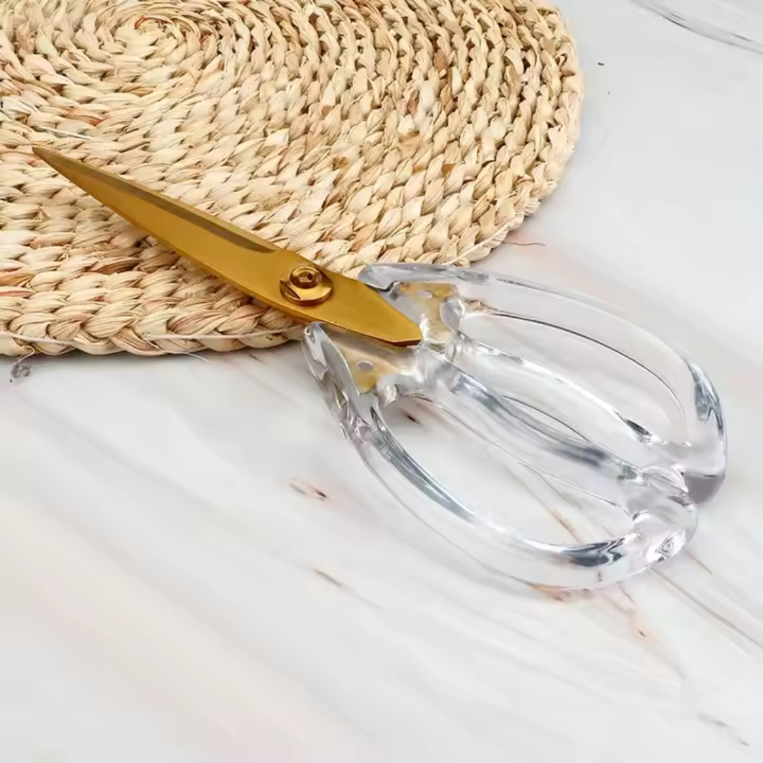 Gold-handled scissors with clear handles on a light wooden surface.