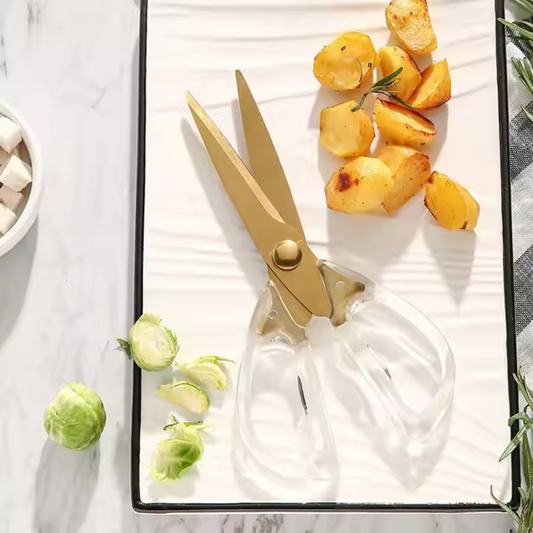 Gold scissors on a white surface with roasted potatoes and brussels sprouts.