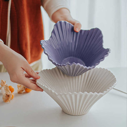 A person is holding a white porcelain embossed serving bowl with a paper fold style design. Another bowl with a purple interior is placed inside it, suggesting the bowl is also available in that color.