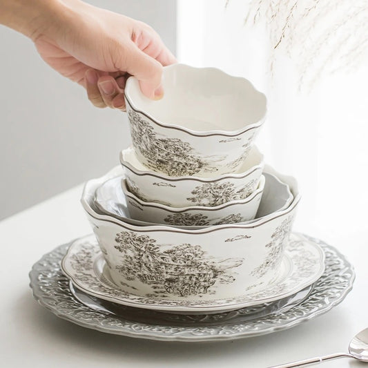 A set of white ceramic Victorian-designed pasta and soup bowls with scalloped edges, featuring a grey print. The bowls are stacked together with a hand reaching out to lift one out of the stack.
