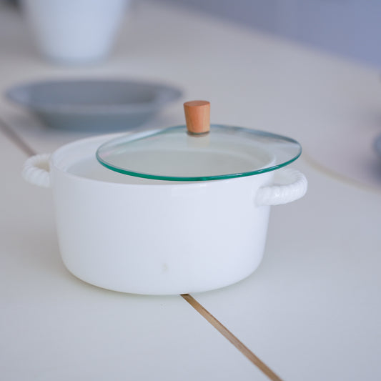 White ceramic casserole pot with glass lid and wooden knob on a tabletop