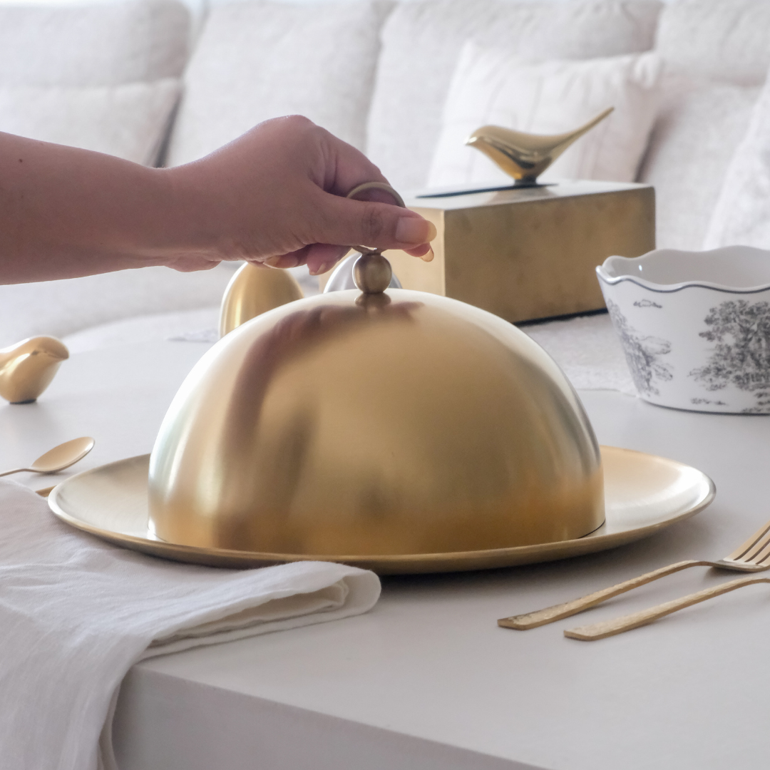 Gold cloche being held over a dish on a table with white background