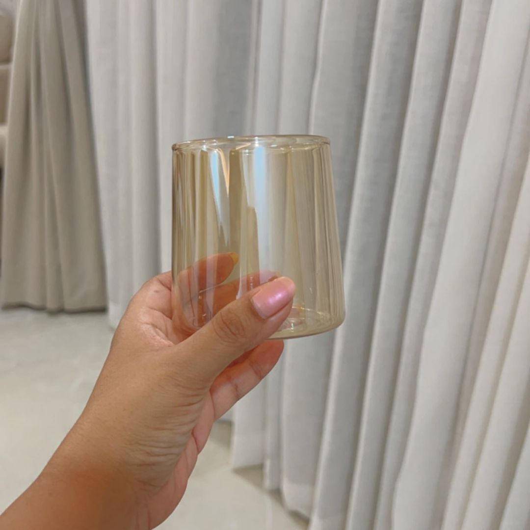 A hand holding a beige amber tinted borosilicate water glass.