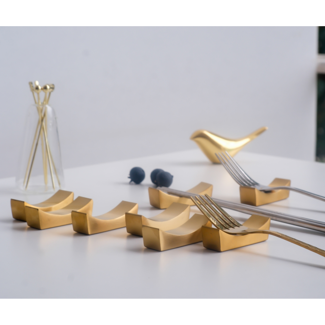 Gold fork and spoon holder on a white surface with a light gray background