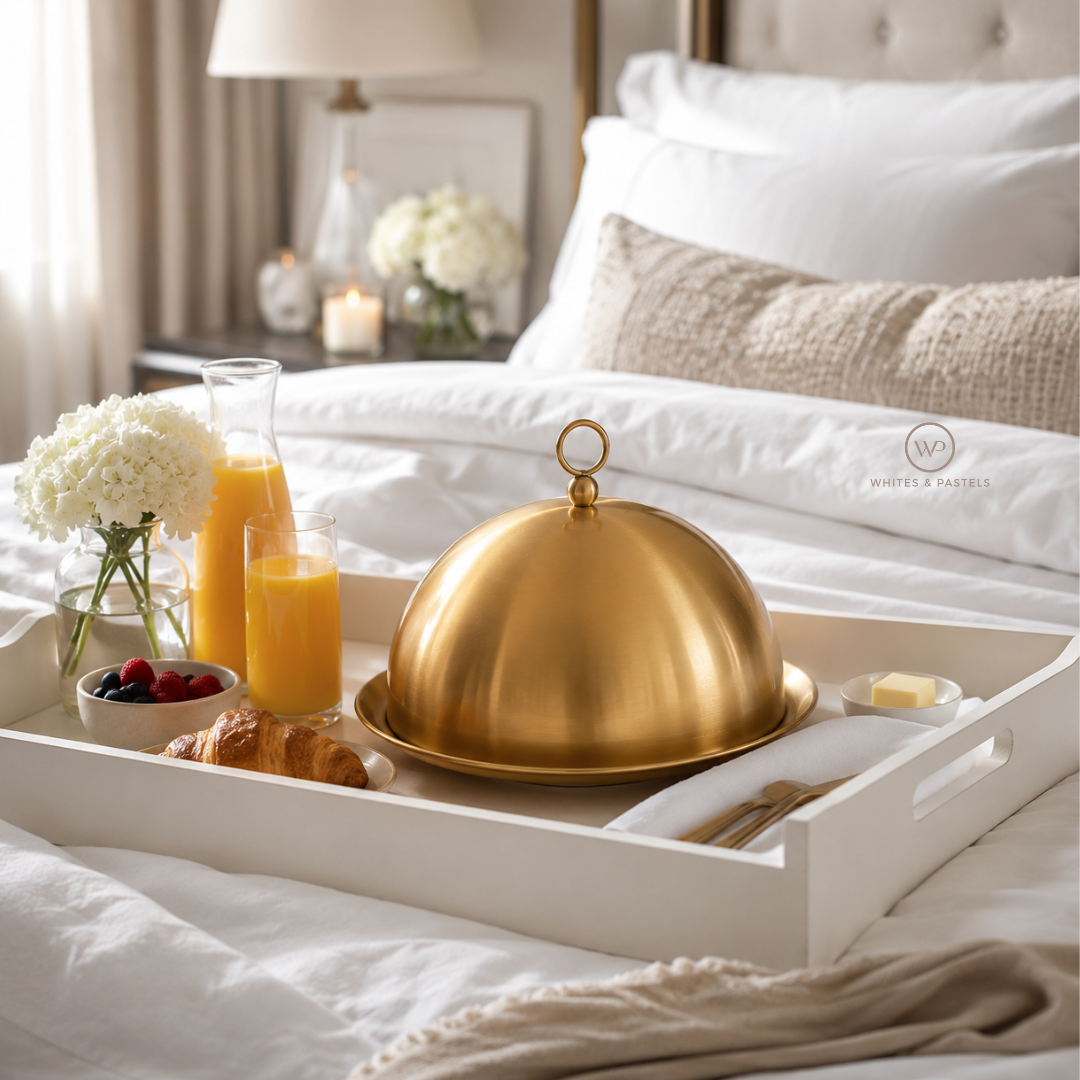 Breakfast tray with gold cloche, orange juice, croissants, and berries on a bed.