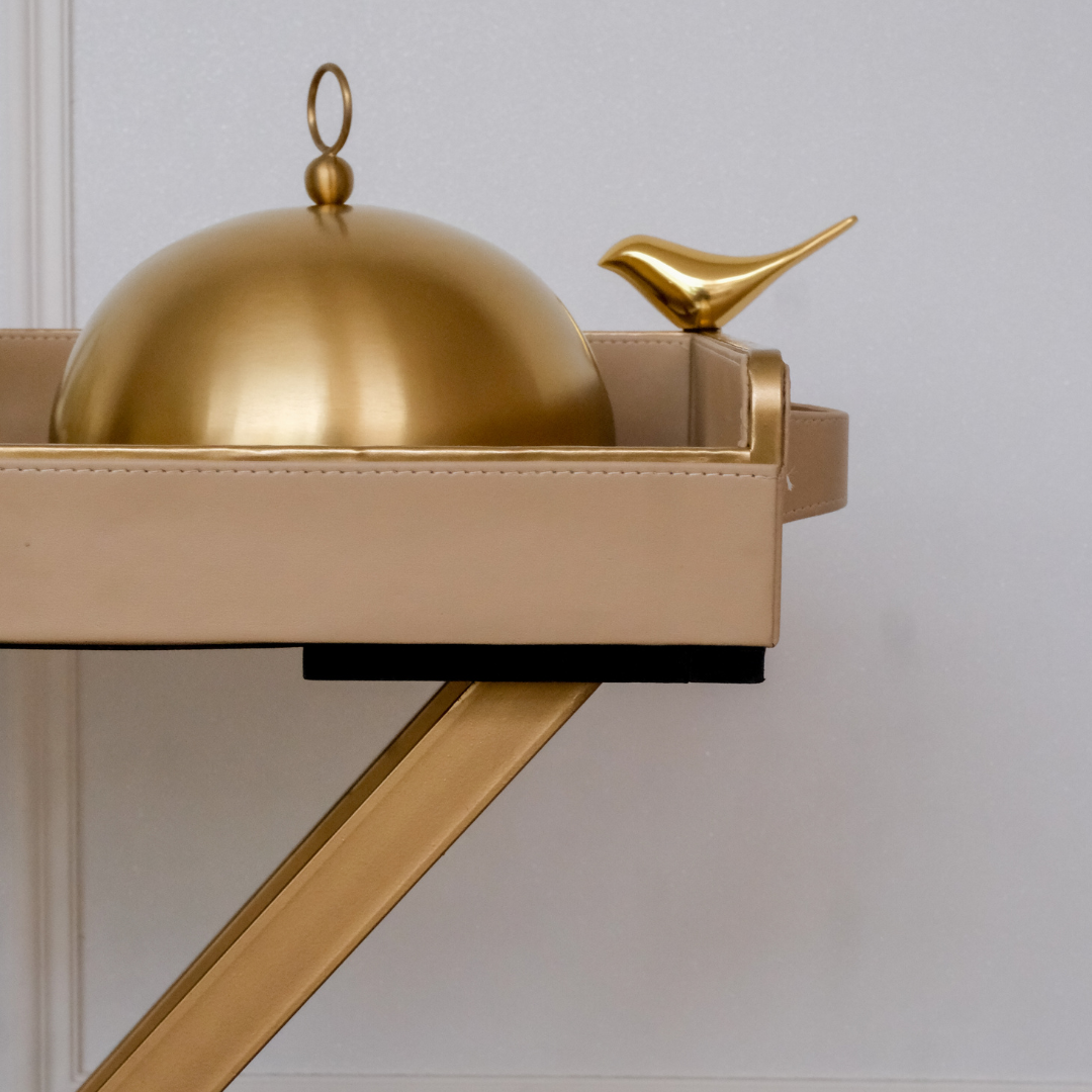 Side profile of a luxury beige butler tray featuring a decorative gold bird handle and premium folding stand.