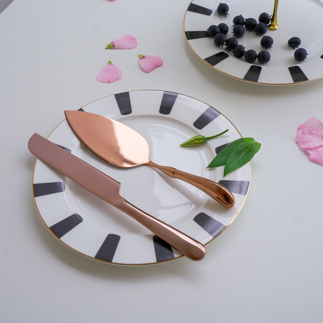 Rose gold knife and spoon on a decorative plate with black and white pattern, surrounded by flowers.