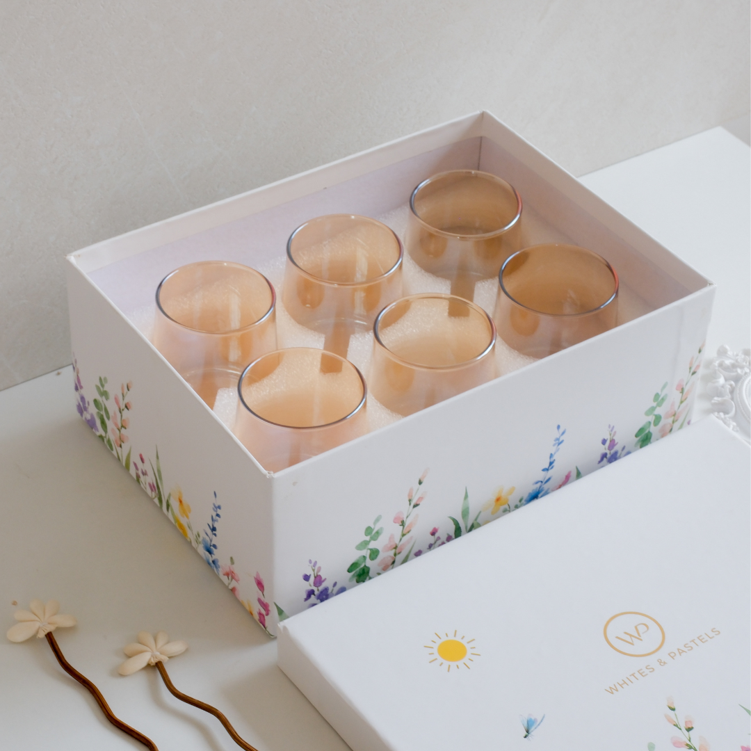 Six brown drinking glasses arranged in front of a luxury Whites & Pastels gift box
