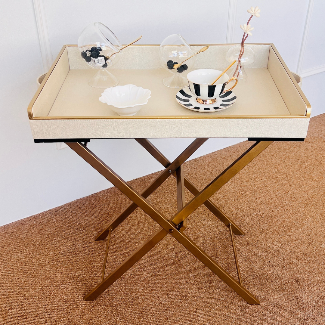 Foldable table with a white butler tray holding decorative items on a brown surface.