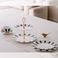 Stylish ceramic high tea serving collection with cake stand, plates, and coffee cup for entertaining guests.