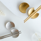 Gold and silver metal chopstick rests on a white surface