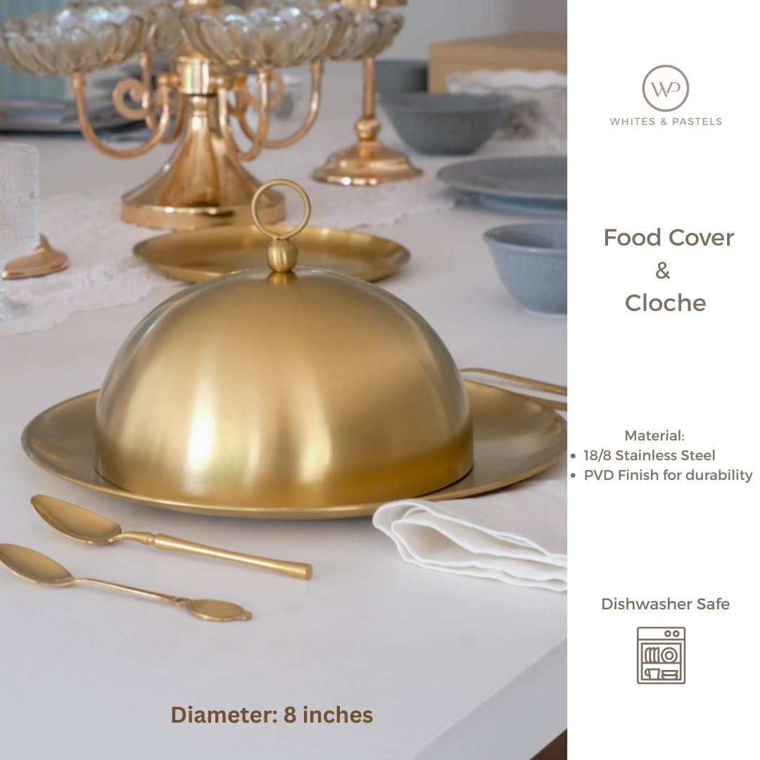 Gold food cover cloche on a table with cutlery and other tableware.
