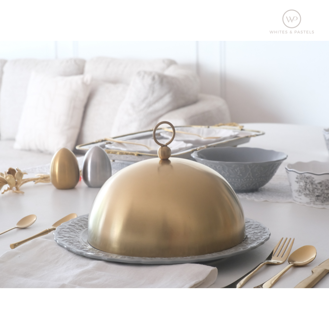 Gold dome-shaped serving dish on a table with silverware and decorative items.