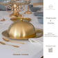 Gold food cover cloche on a table with cutlery and other tableware.