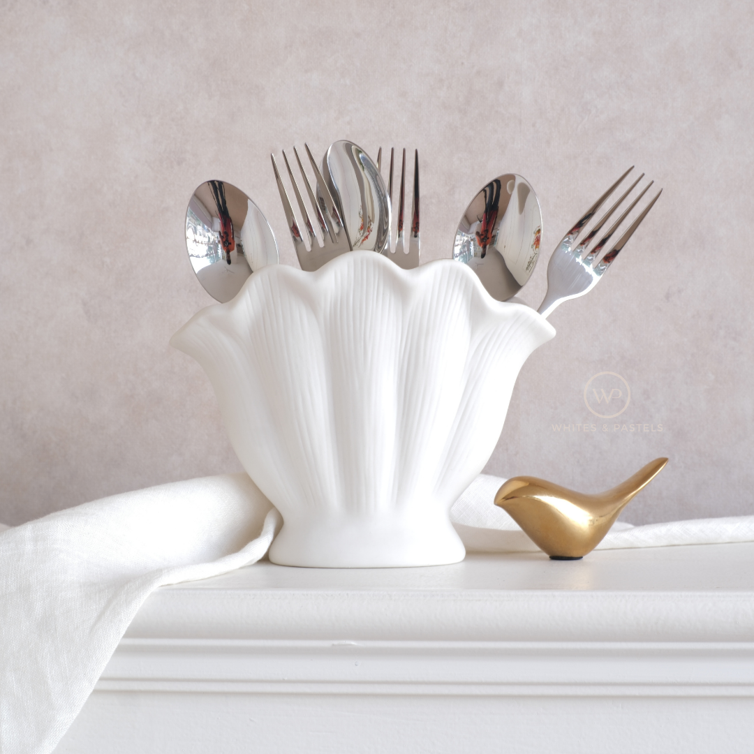 Silver cutlery set in a white shell-shaped holder on a light surface with a gold bird