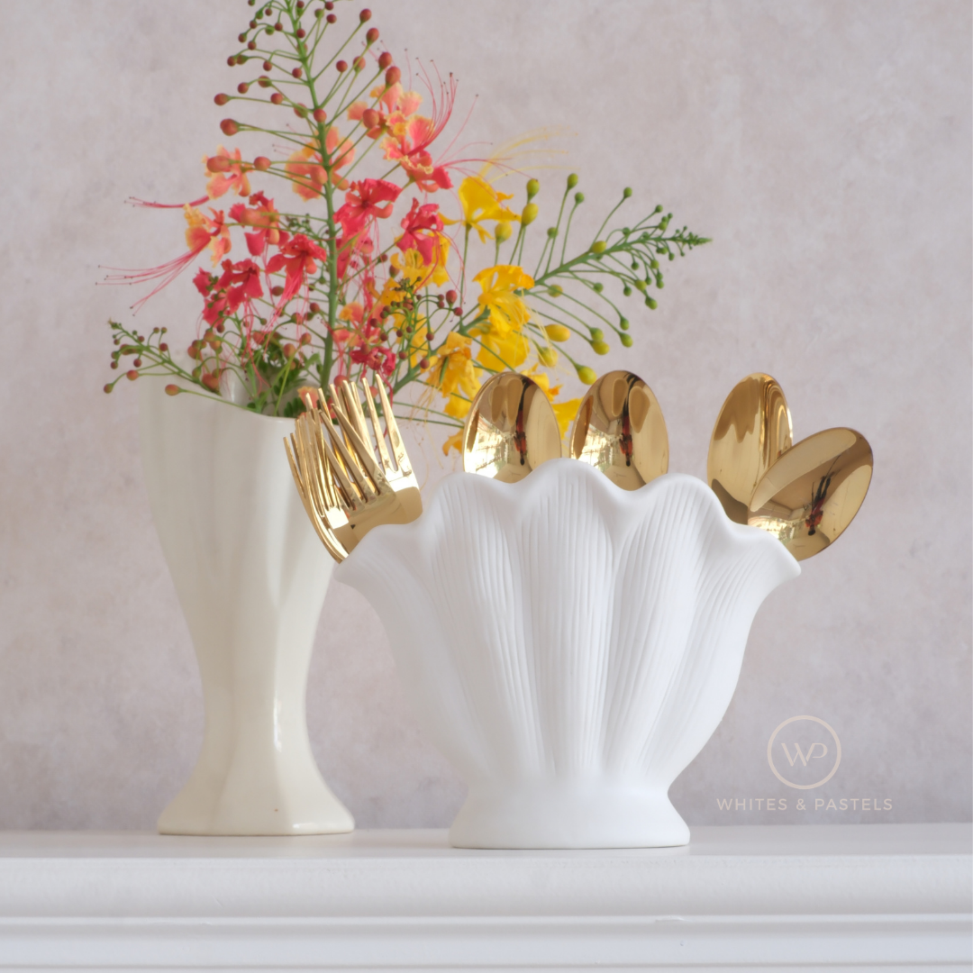 Decorative shell-shaped vase and cutlery holder with gold spoons inside and a bouquet of flowers on the side