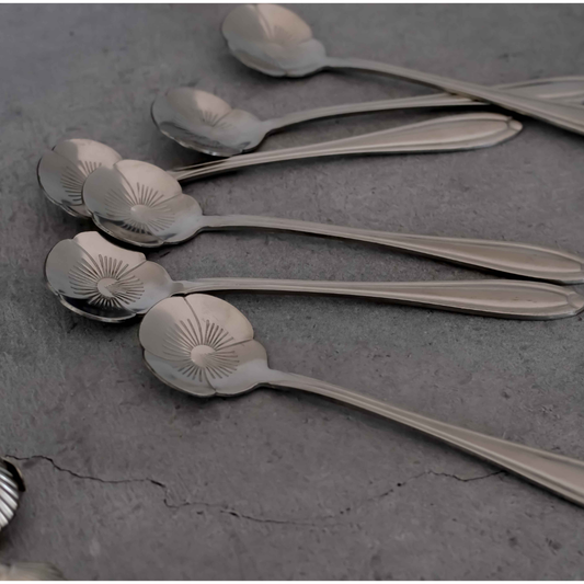 Stainless Steel silver metal spoons with decorative flower-shaped bowls, arranged diagonally on a textured gray surface.