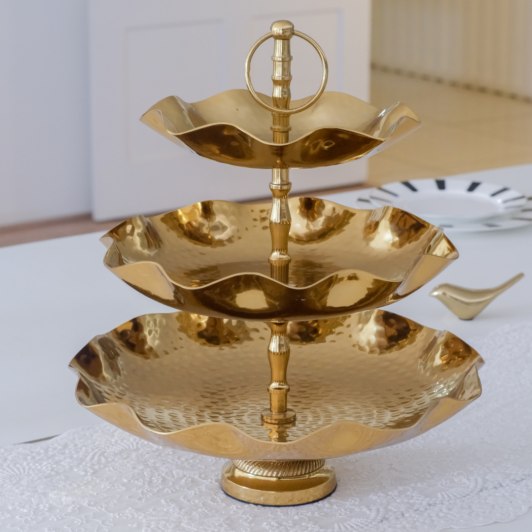 Three-tiered gold serving tray on a white surface with a neutral background