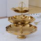 Three-tiered gold serving tray on a white surface with a neutral background