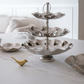 Three-tiered silver decorative tray on a white surface with a blurred background