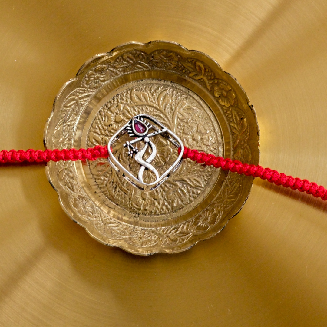 Premium Pure Silver Rakhi showcasing an elegant dancing Krishna design with a decorative ruby-red stone on a traditional red braided thread.