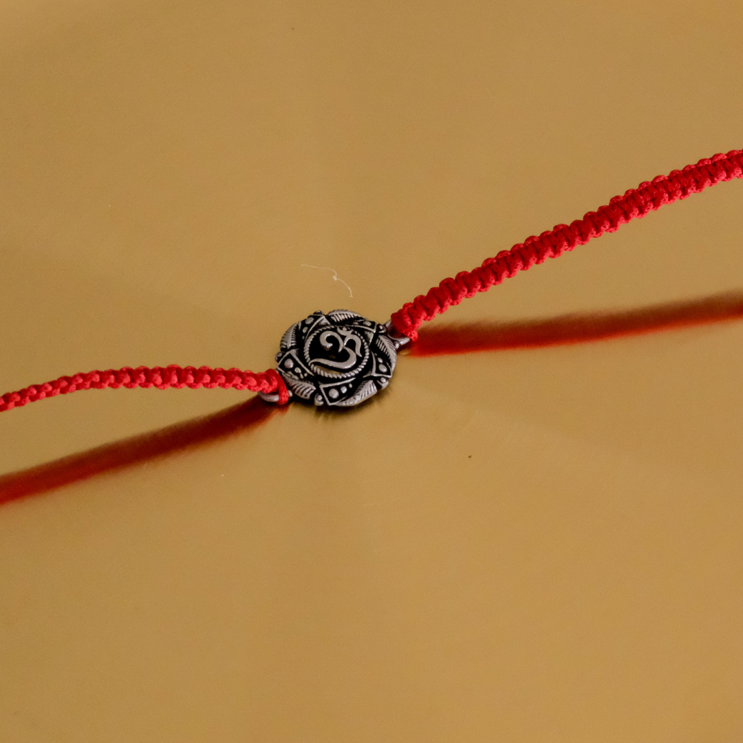 Close-up of a handcrafted Pure Silver Om Rakhi featuring an elegant silver Om symbol on a traditional red thread.