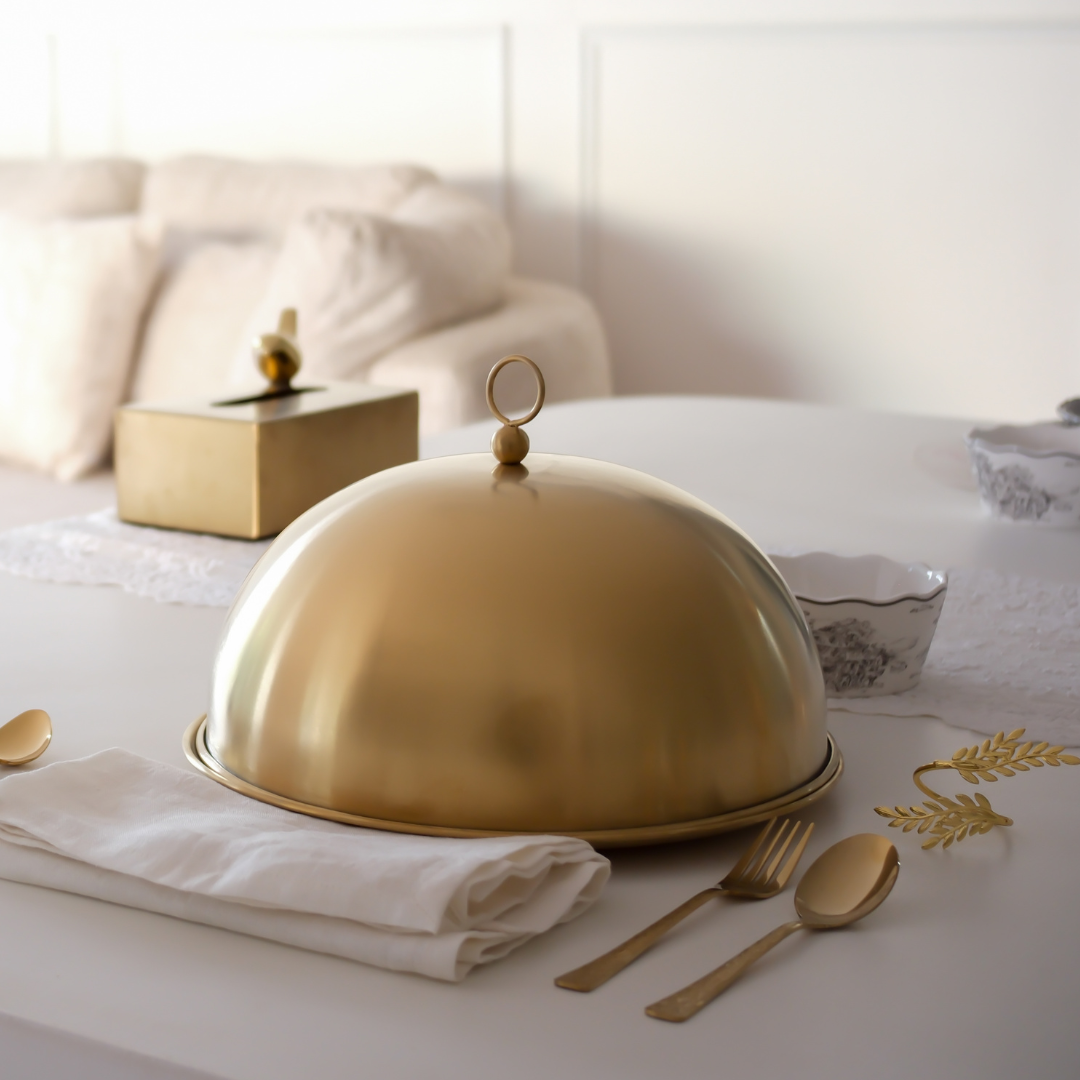 Gold cloche on a table with white tablecloth and gold cutlery