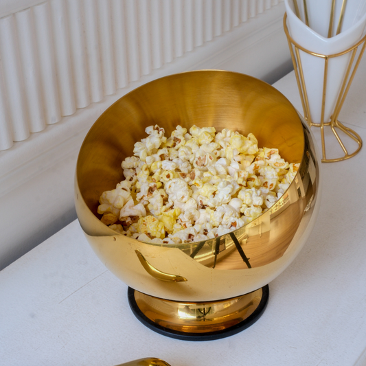 Modern contemporary gold serving bowl with popcorn on a minimalist white tabletop.
