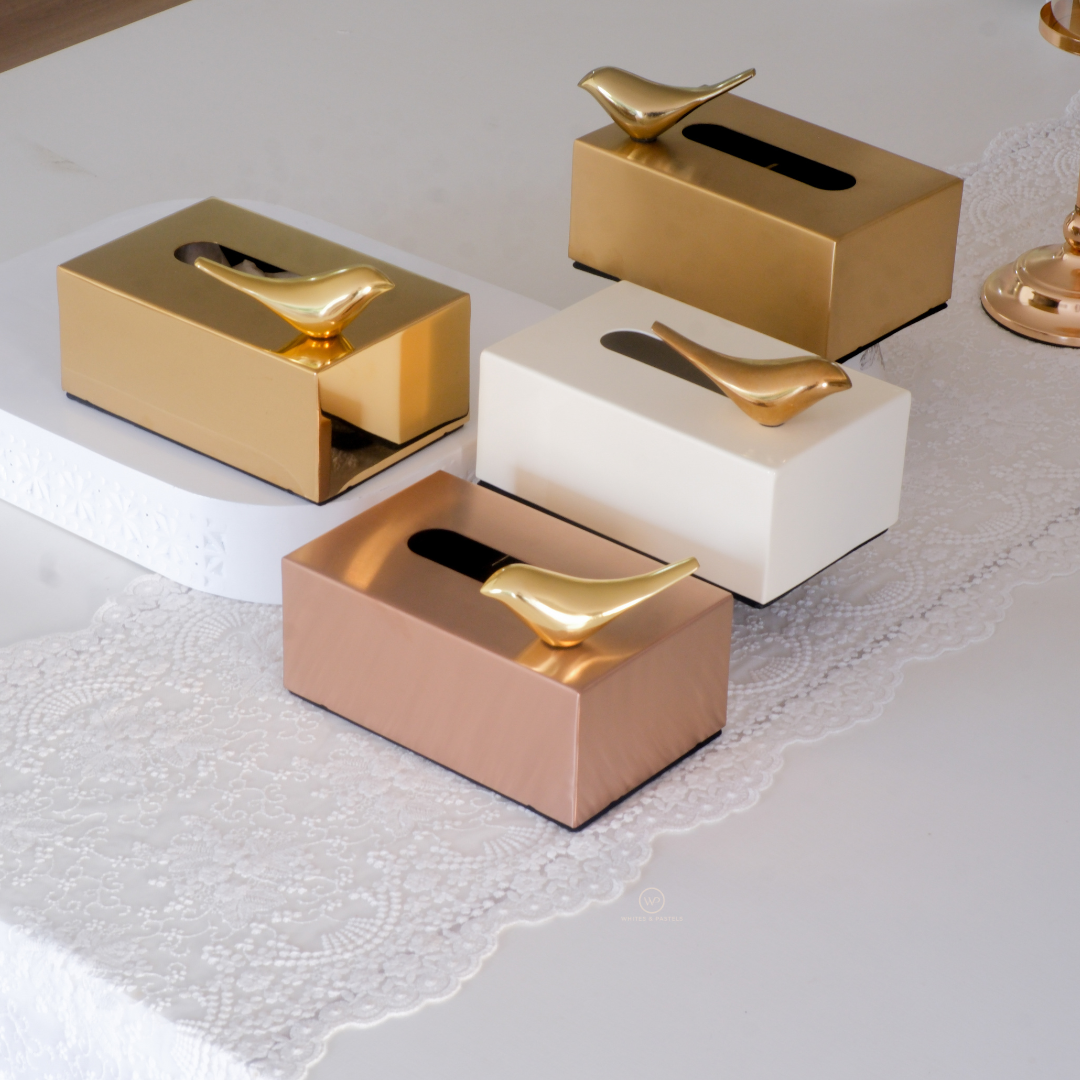 Luxury metallic tissue box with decorative bird accent in gold, rose gold and ivory finishes displayed on an elegant tabletop