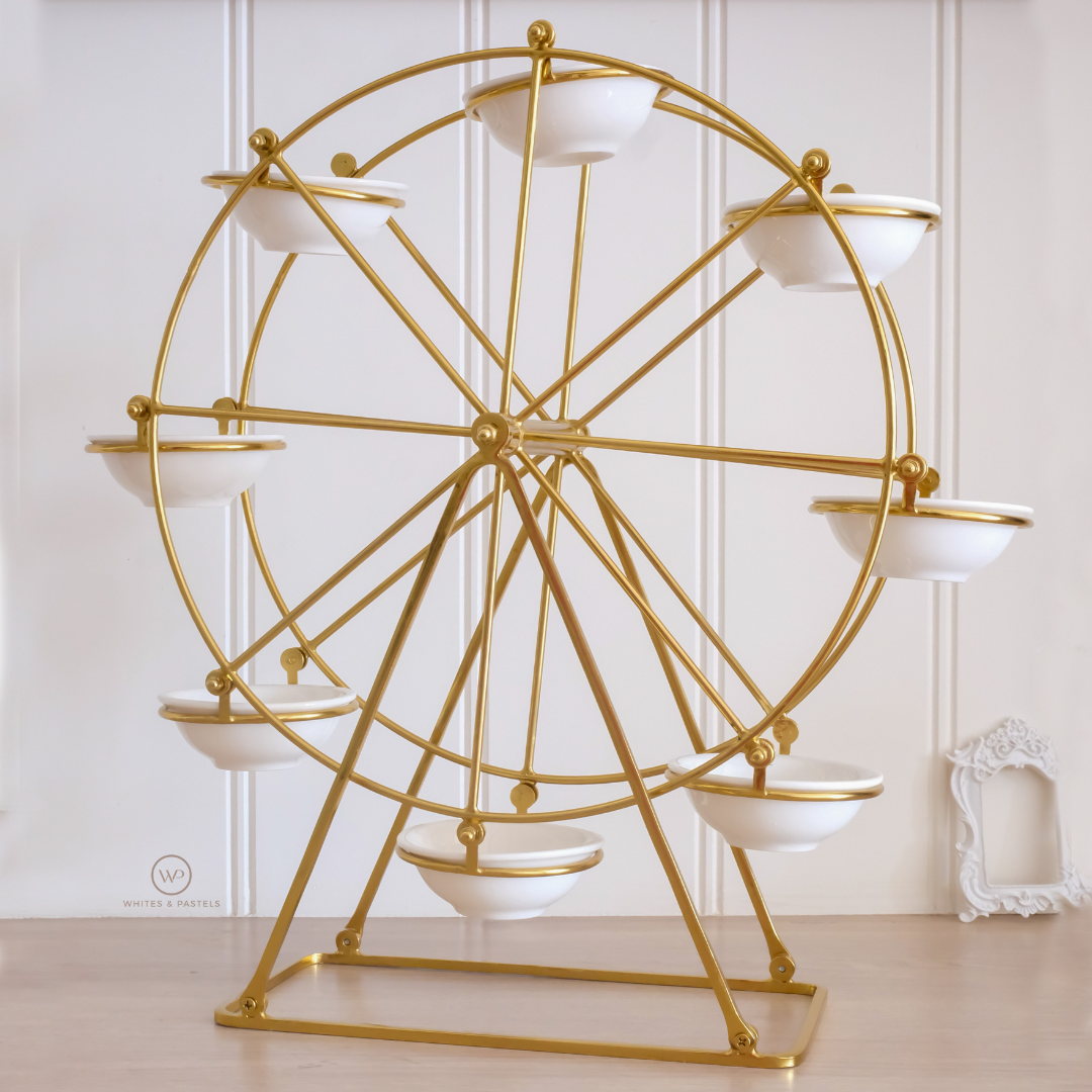 A gold metal Ferris wheel decorative stand with eight white ceramic bowls, set against a white paneled wall and light wood floor.