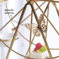 Close-up of a gold metal food display stand with a butterfly-shaped ornament attached to one of its arms. The image includes a text callout reading 'Butterfly detailing and a small logo near the bottom that say Whites & Pastels.
