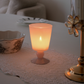 Tea light candle holder in a frosted glass goblet shape vase with a warm peach-orange glow, placed on a lace table runner on a tabletop in a softly lit interior setting.