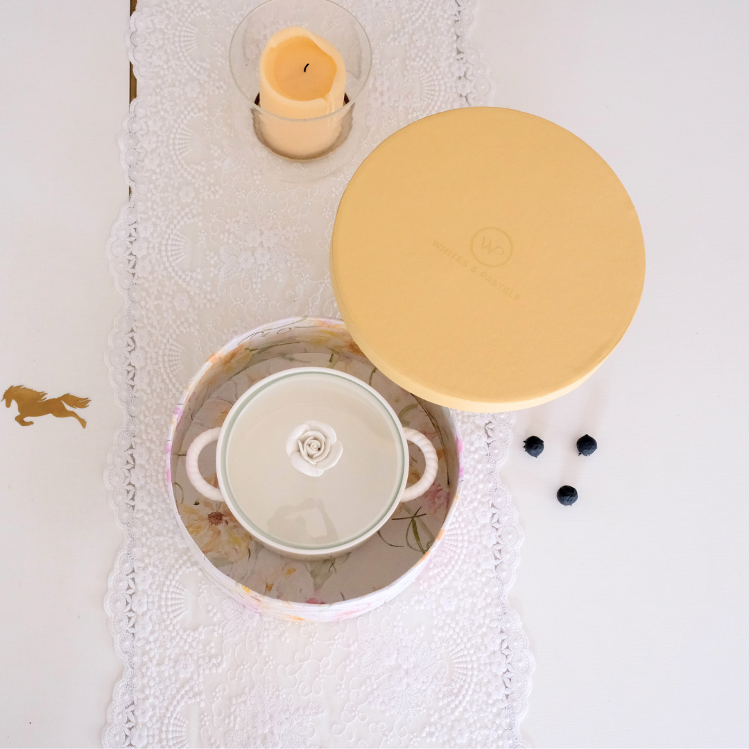 Festive giftbox with serving bowl on a white runner with a a hurricane holder nearby