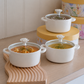 Three white ceramic soup pots with floral lid knobs are arranged on a light wood surface. These pots are filled with soup, curry and dal.