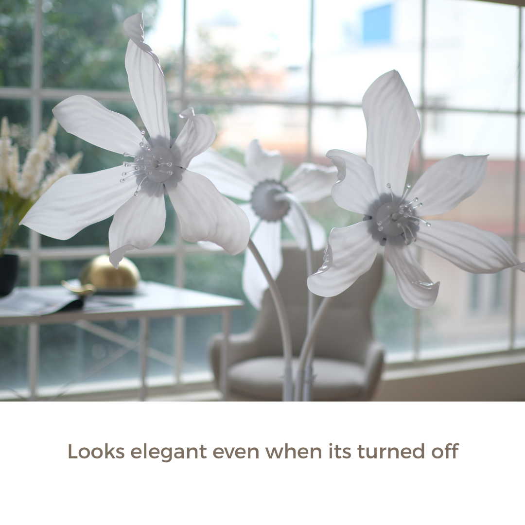 White artificial flower-like decor pieces displayed indoors near a window, with a chair and table in the softly blurred background. Text at the bottom reads, 'Looks elegant even when its turned off.