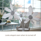 White artificial flower-like decor pieces displayed indoors near a window, with a chair and table in the softly blurred background. Text at the bottom reads, 'Looks elegant even when its turned off.