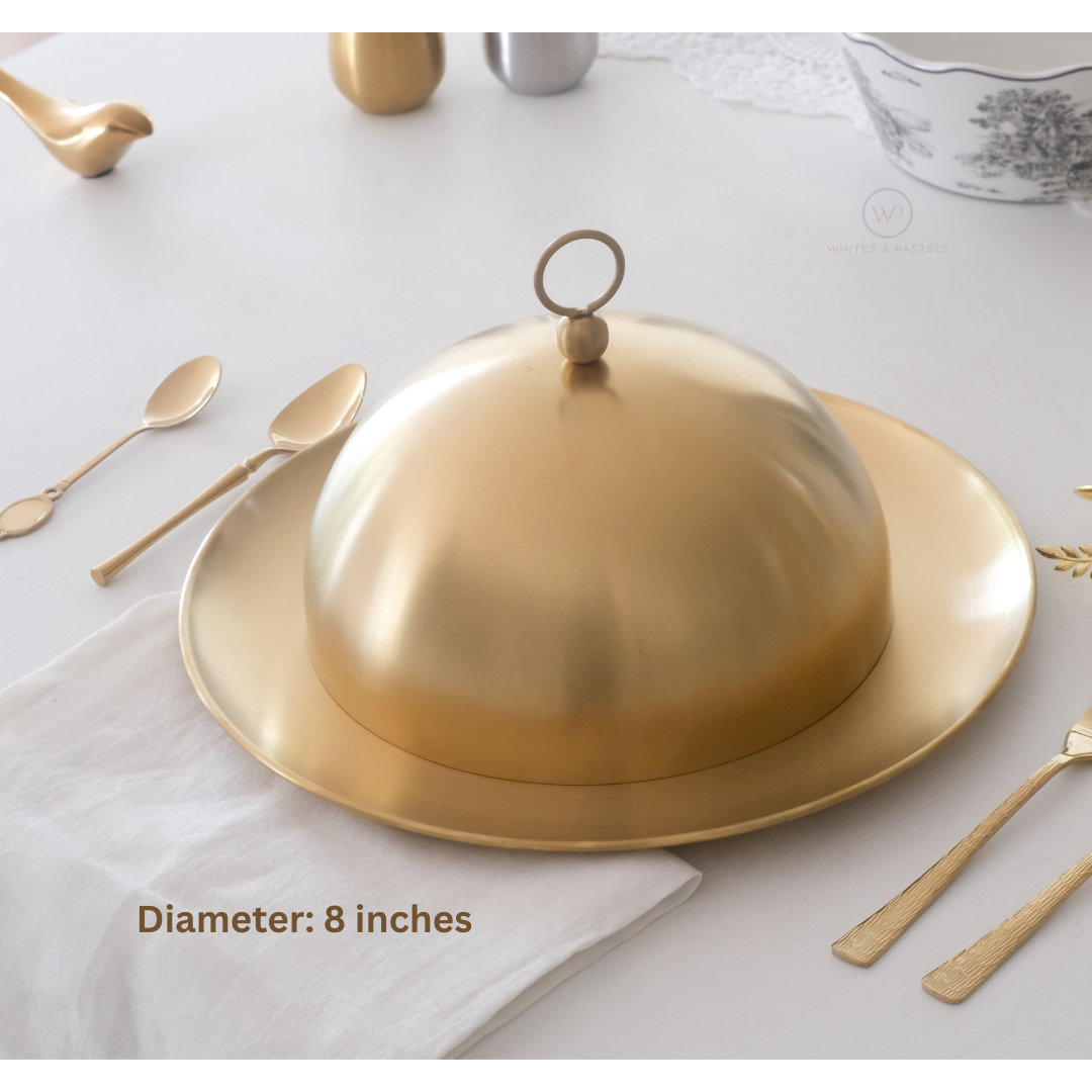 Gold platter with dome lid on a white surface with utensils