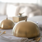 Two gold cloche dishes on a table with a blurred background