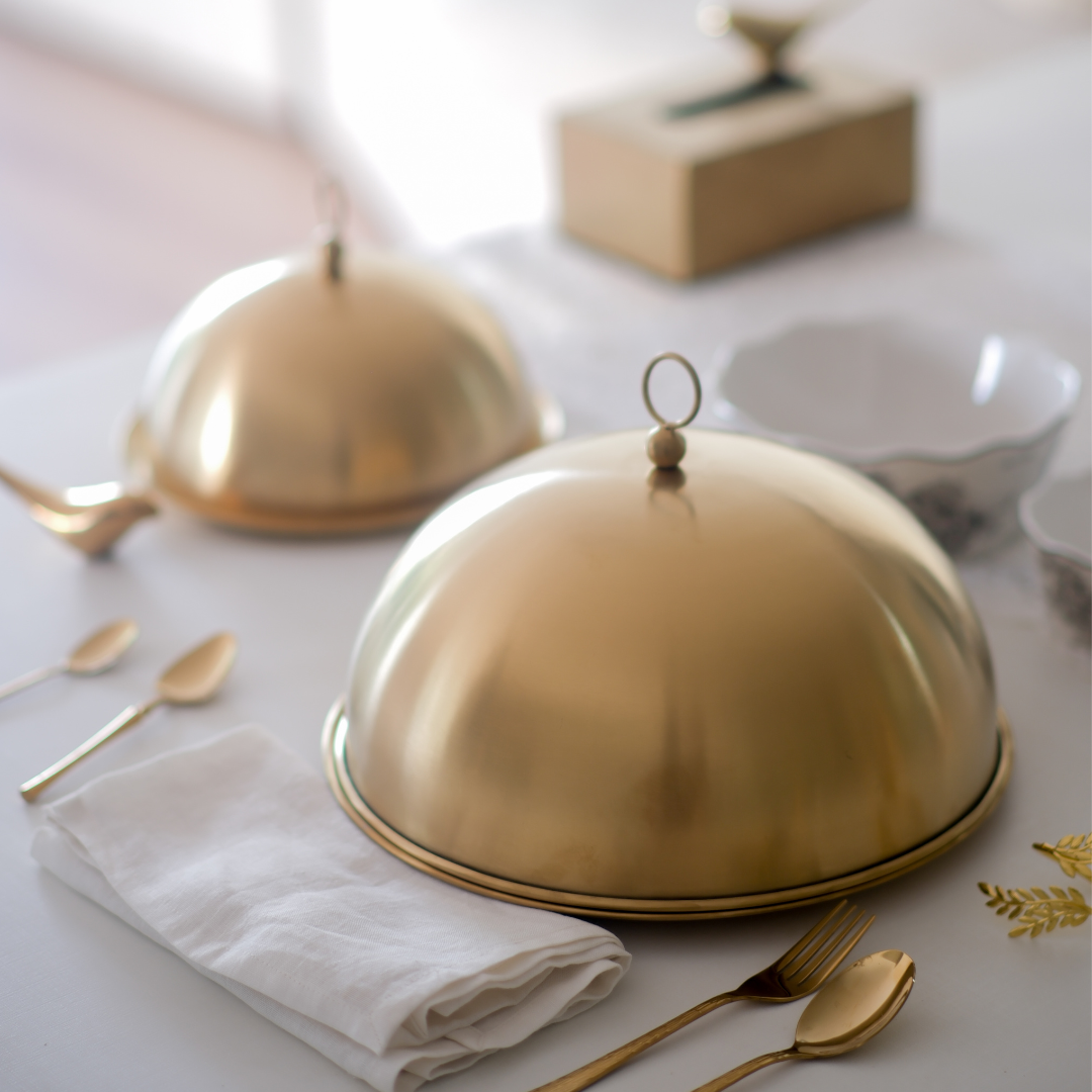 Gold cloche dishes on a table with white napkins and gold utensils.