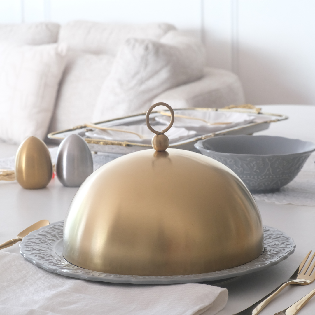 Gold serving dome on a decorative platter with a white background