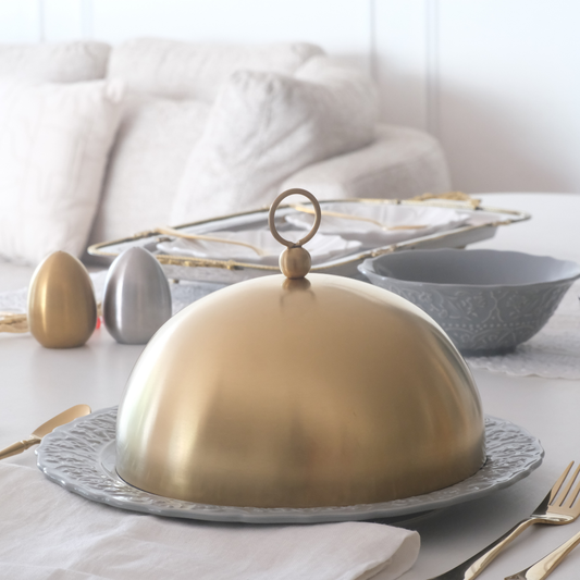 Gold serving dome on a decorative platter with a white background