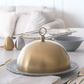 Gold serving dome on a decorative platter with a white background