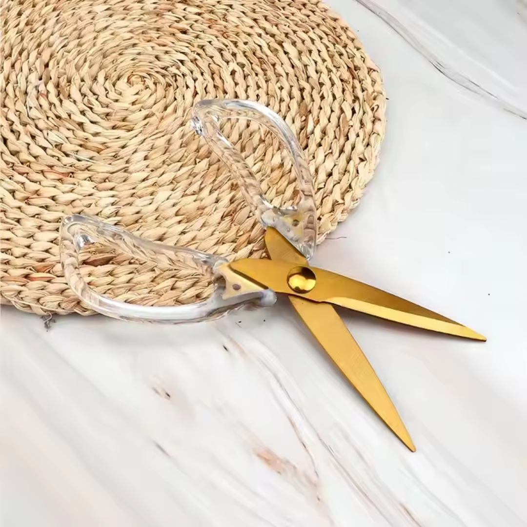 Gold scissors with clear handles on a marble surface
