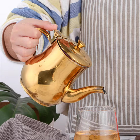 A person lifting a gold stainless steel tea pot with a mirror finish, preparing to pour liquid into a cup.