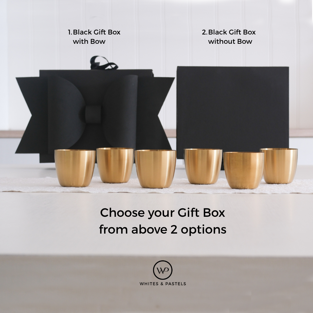 Six small metallic gold cups are arranged on a white surface in front of two black gift boxes, one with a large bow and one plain. Text reads '1.