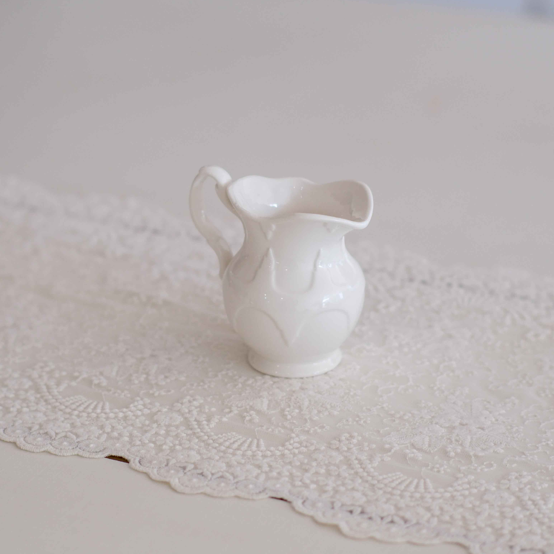 Elegant ivory ceramic milk creamer pitcher with embossed Victorian design and curved handle, ideal for serving milk, cream, syrup or sauces.