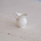 Elegant ivory ceramic milk creamer pitcher with embossed Victorian design and curved handle, ideal for serving milk, cream, syrup or sauces.
